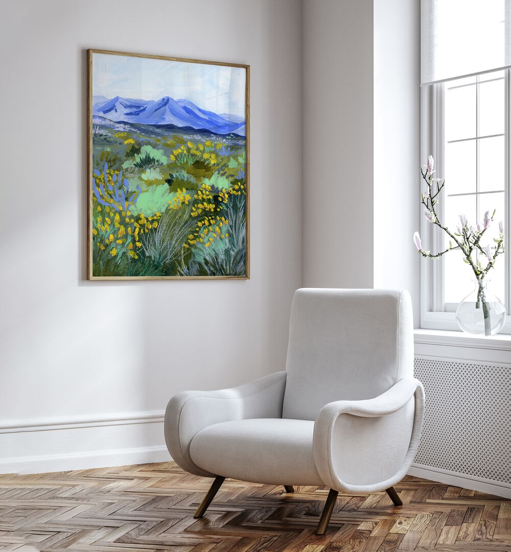 Blue Valley By Sarah Gesek Landscape Art Prints in Oak Wood Plain Frame placed on a white wall beside a white chair and a window