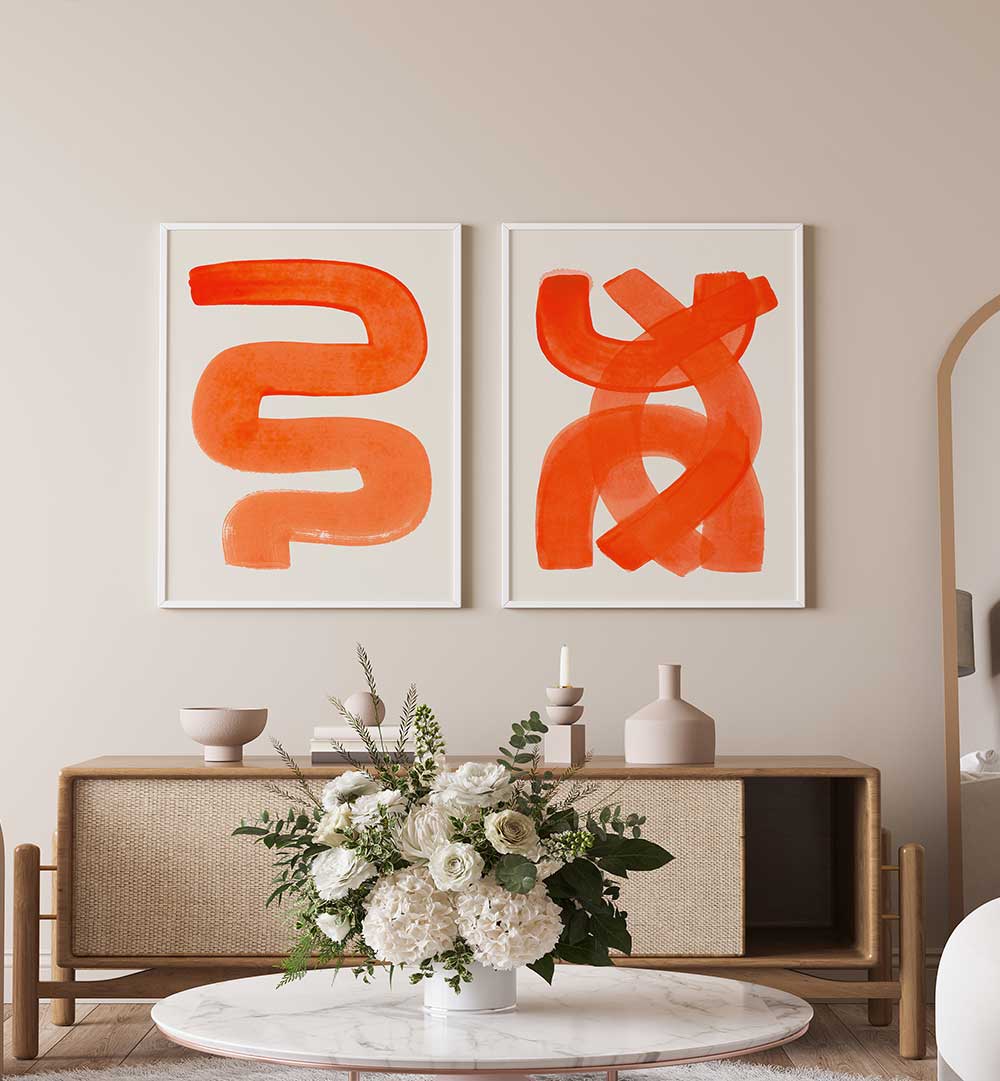 Two abstract orange artworks on a beige wall above a wooden console table with decorative items.