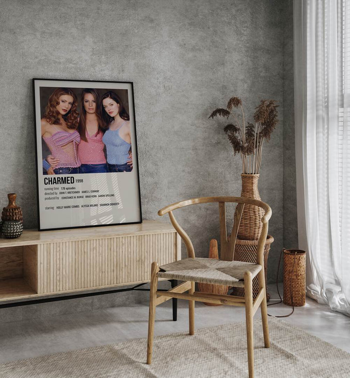 Charmed 1998 Movie Posters in Black Plain Frame placed on a table beside oakwood chair