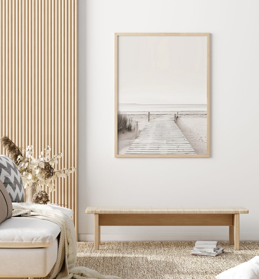 Coastal Cove Path Beach Prints Coastal Wall Art in Oak Wood Plain Frame placed on a wall behind a table and beside a sofa