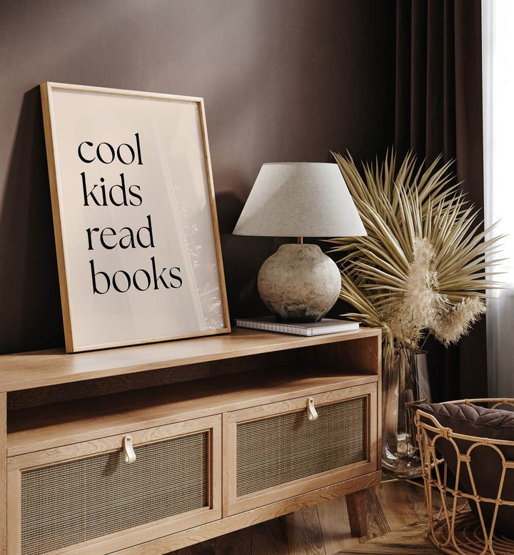 Cool Kids Read Books by Anne-marie Volfova Quotes and Typography Posters in Oak Wood Plain Frame placed on a console table beside a lamp