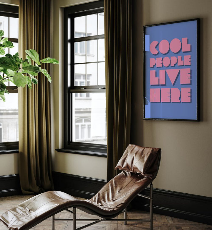 Cool People Live Here by Athene Fritsch Quotes and Typography Posters in Black Plain Frame placed on a living room wall behind a chair and beside a window