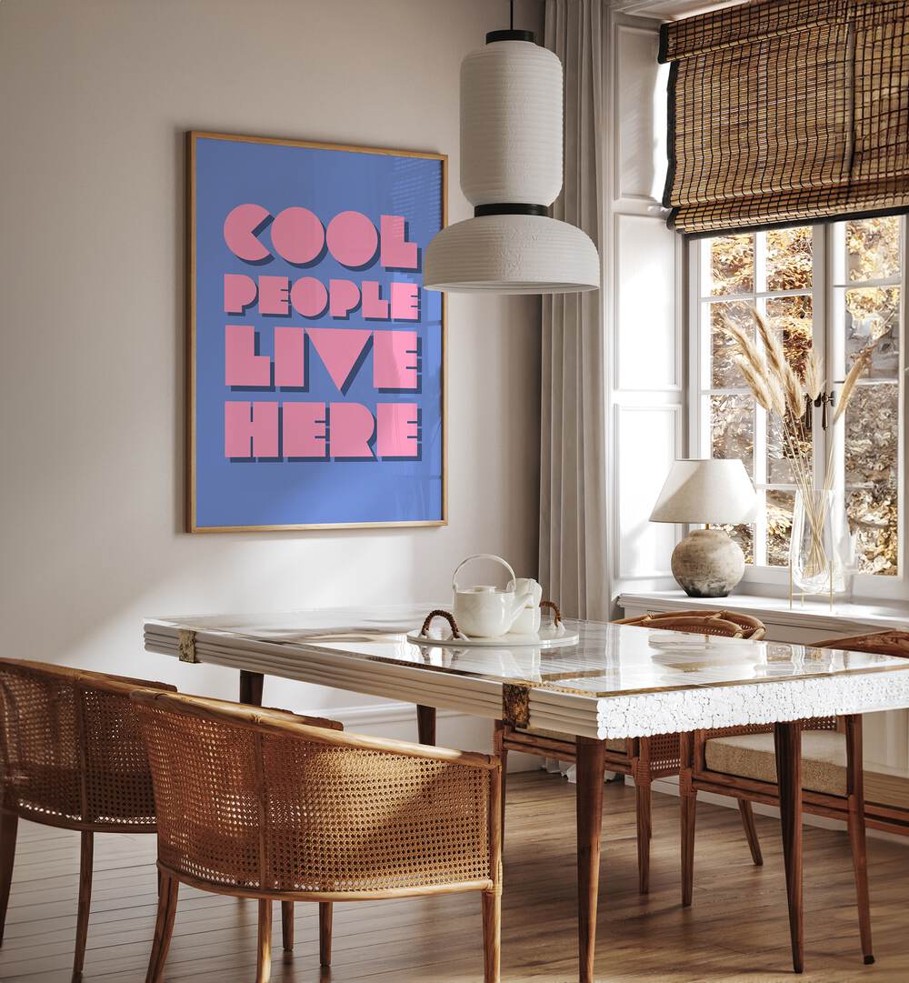 Cool People Live Here by Athene Fritsch Quotes and Typography Posters in Oak Wood Plain Frame placed on a wall in a dining room area beside a window and behind a dining table