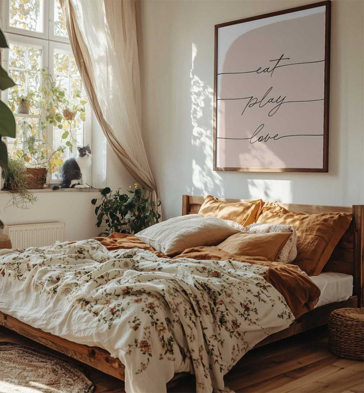 Cozy bedroom with framed EAT PLAY LOVE , QUOTES poster above bed, floral bedding, plants and cat on windowsill
