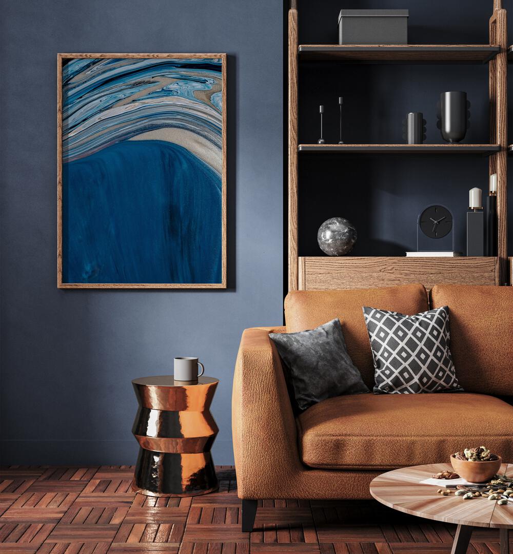 Ebb and Flow Beach Prints Coastal Wall Art in Oak Wood Plain Frame placed on a blue wall beside a sofa