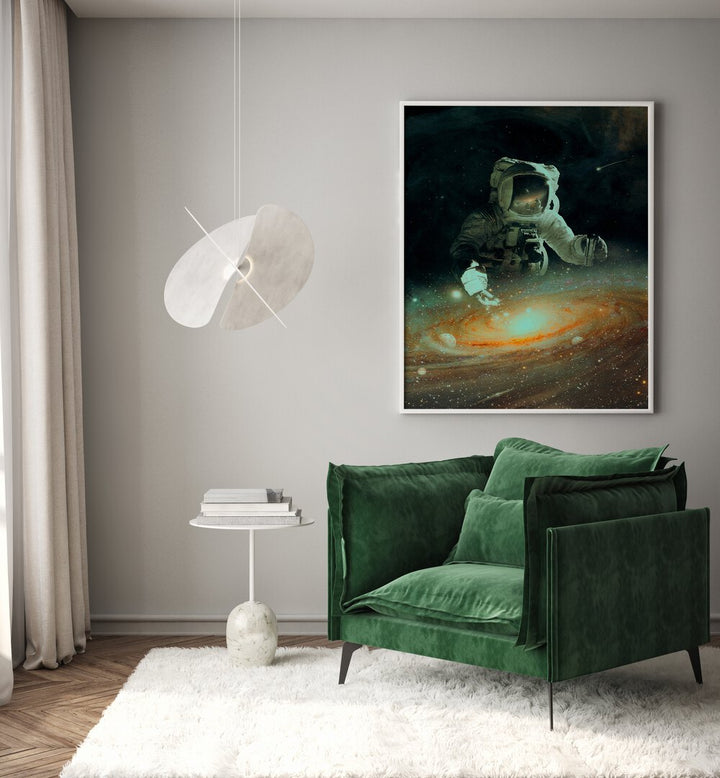 Feeding The Abyss By Francis Minoza Astronaut & Nasa Paintings, Space Art Prints Artwork in White Plain Frame placed on a Grey Colored Wall near a Green Sofa Chair in the Drawing Room
