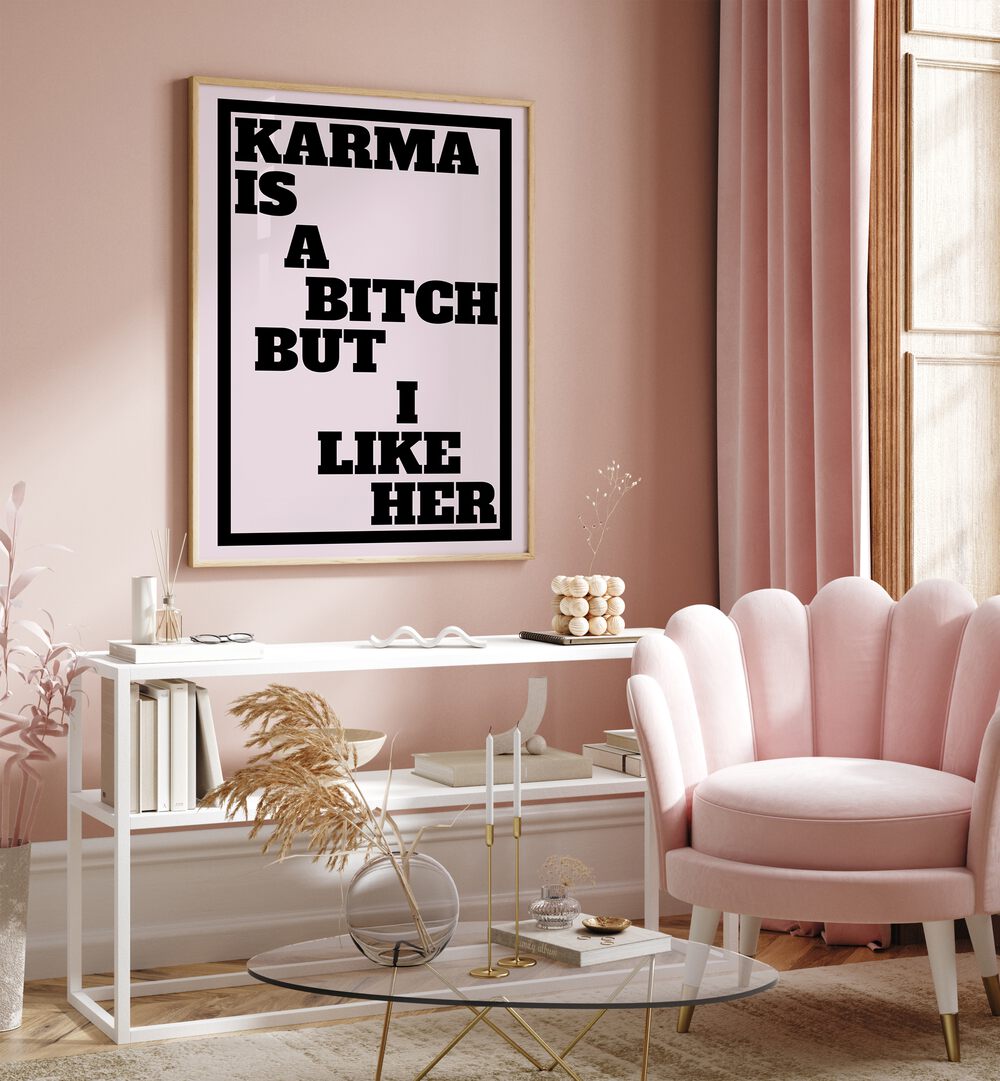 Karma is a Bitch by Athene Fritsch Quotes and Typography Posters in Oak Wood Plain Frame placed on a pink wall beside a window and behind a table