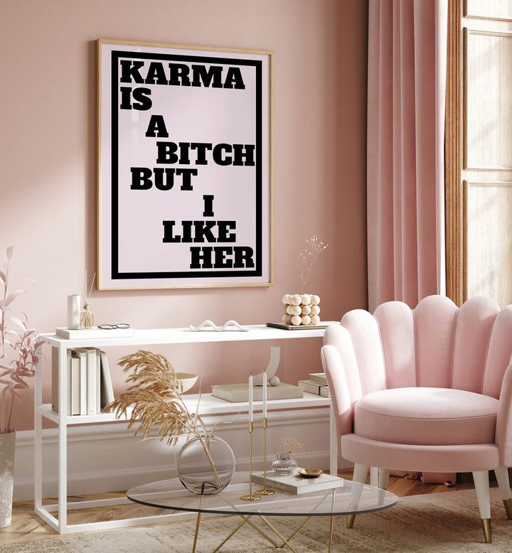 Karma is a Bitch by Athene Fritsch Quotes and Typography Posters in Oak Wood Plain Frame placed on a pink wall beside a window and behind a table