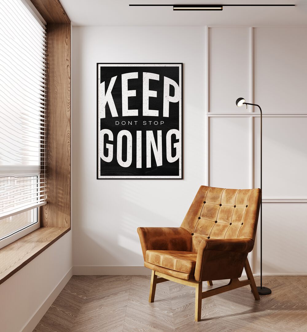 Keep Going Dont Stop Quotes And Typography Posters in Black Plain Frame placed on a Cream Colored Wall near a Brown Sofa Chair in the Drawing Room