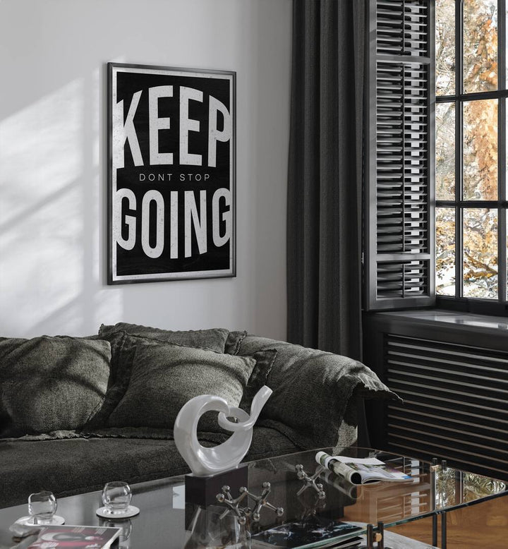 Keep Going Dont Stop Quotes And Typography Posters in Black Plain Frame placed on a White Colored Wall near a Grey Sofa in the Living Room