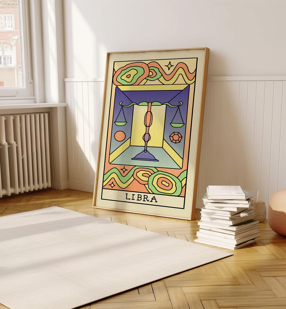 Libra Zodiac & Tarot Art Painting Artwork in plain oakwood frame on a wooden floor beside a stack of books