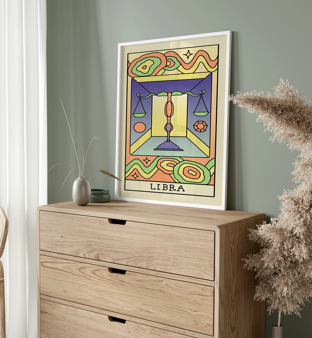 Libra Zodiac & Tarot Art Painting Artwork in plain white frame on a console table beside a plant