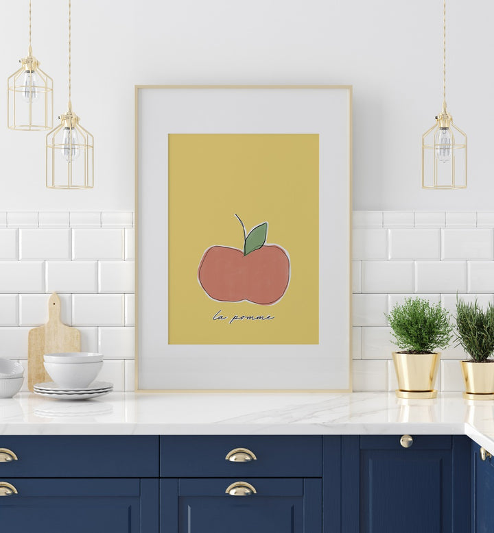 La Pomme by Uplus Me Studio Kitchen Art Prints Kitchen Posters in White Frame With Mount placed on a kitchen counter for kitchen area