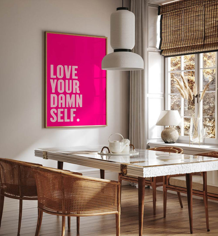 Love Your Damn Self by Athene Fritsch Quotes and Typography Posters in Oak Wood Plain Frame placed on a wall in a dining room area beside a window and behind a dining table