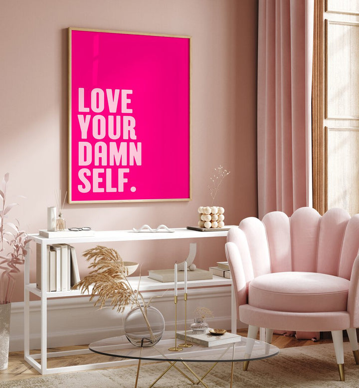 Love Your Damn Self by Athene Fritsch Quotes and Typography Posters in Oak Wood Plain Frame placed on a pink wall beside a window and behind a table