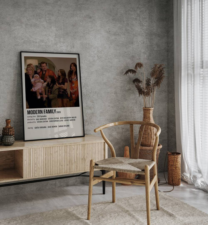 Modern Family 2009 Movie Posters in Black Plain Frame placed on a table beside oakwood chair
