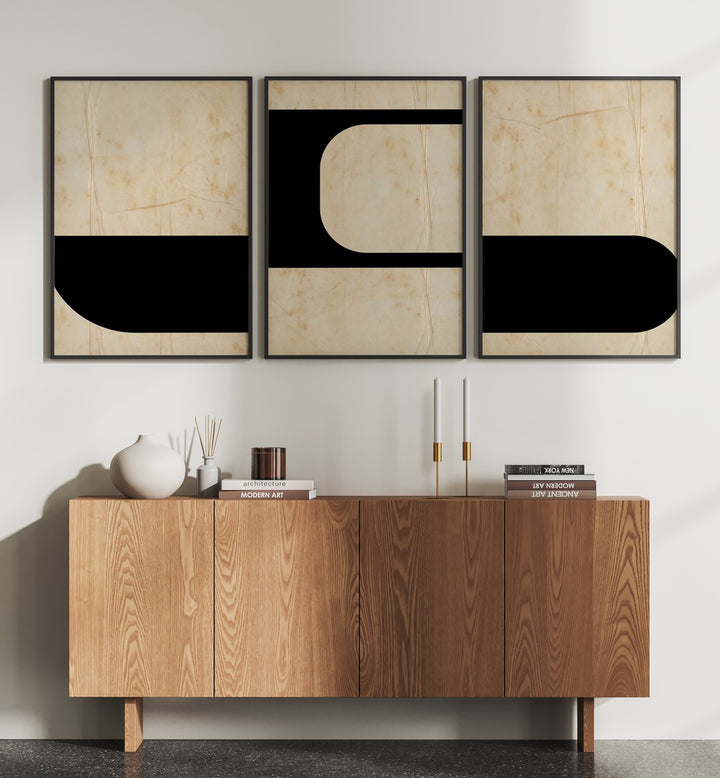 Modern Geometric Set Set Of 3 Paintings in Black Plain Frame placed on a white wall behind a brown table