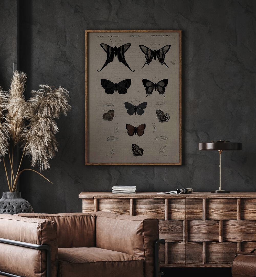 Mystical Moths Wings Of Night's Embrace Gothic Art Prints in Oak Wood Plain Frame hanging on wall above brown chair beside plant.