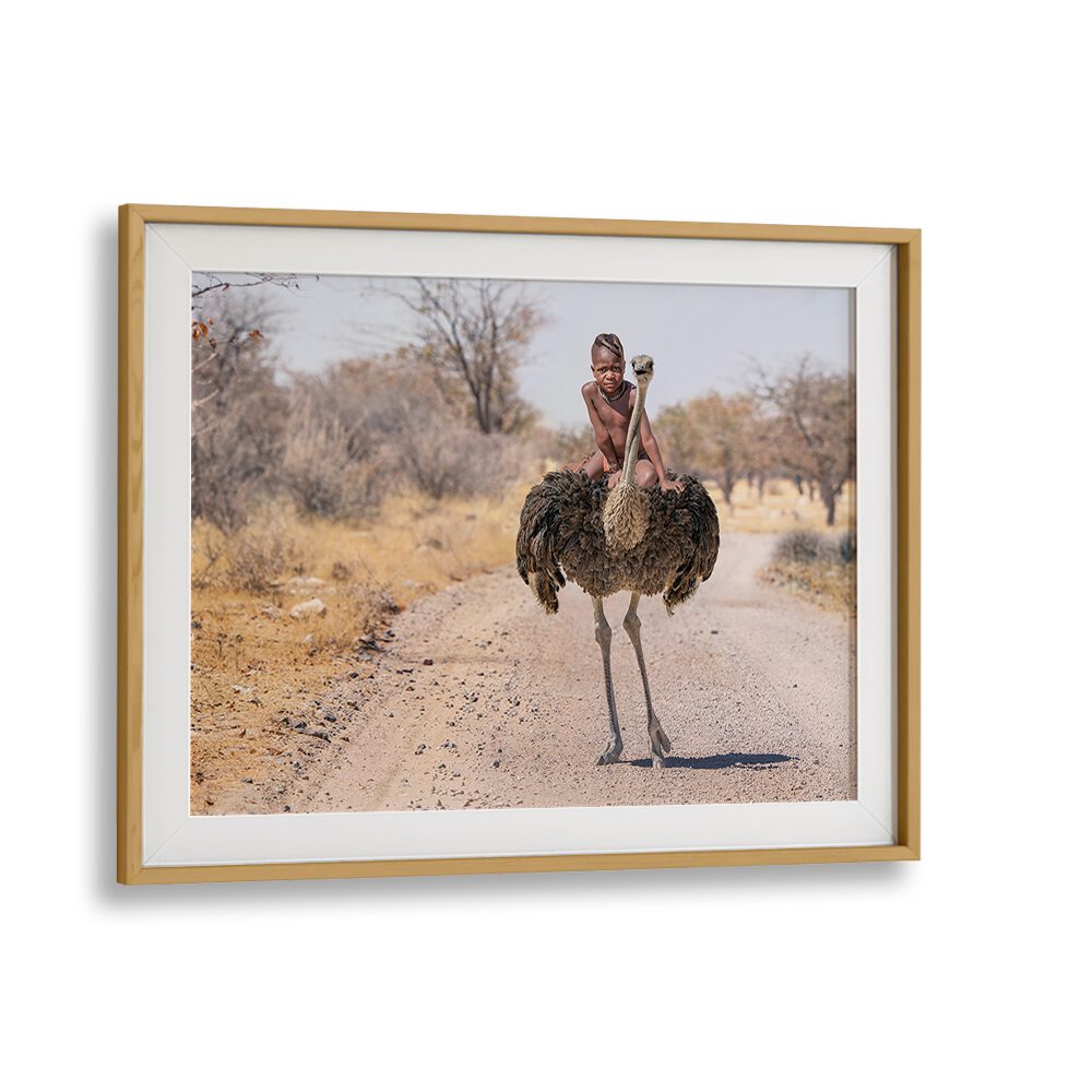 A young boy rides an ostrich on a dirt path, showcasing HIMBA RIDE, PHOTOGRAPHY PRINTS for unique wildlife art.