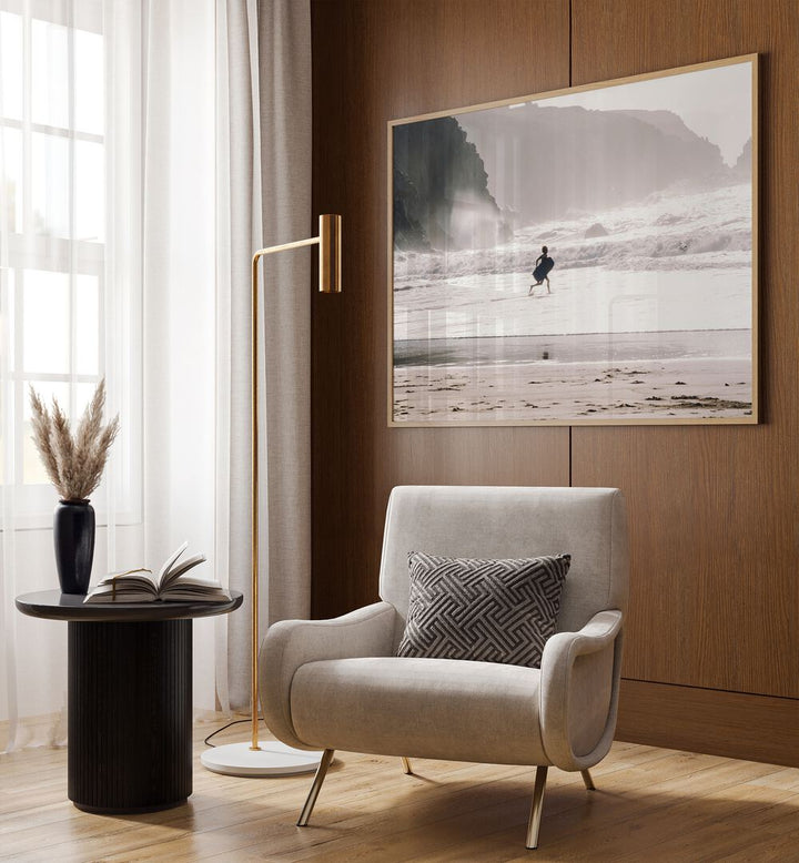 Oceans Call Beach Prints Coastal Wall Art in Oak Wood Plain Frame placed on a wall behind a chair