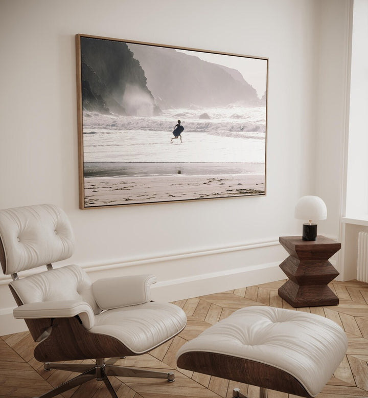 Oceans Call Beach Prints Coastal Wall Art in Oak Wood Floater Frame placed on a wall beside a chair