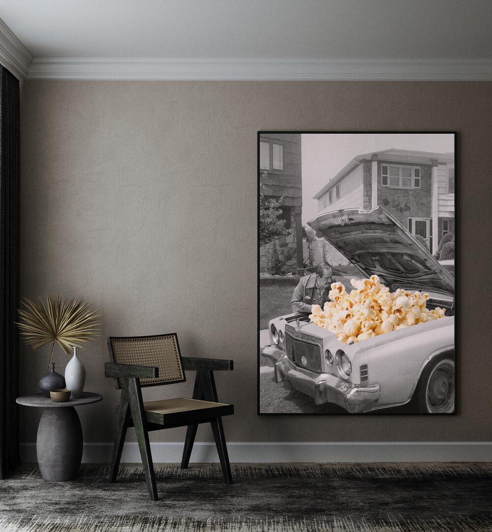 Pop The Hood Popcorn Car Surreal Art Painting Artwork in plain black frame beside a chair on a beige wall