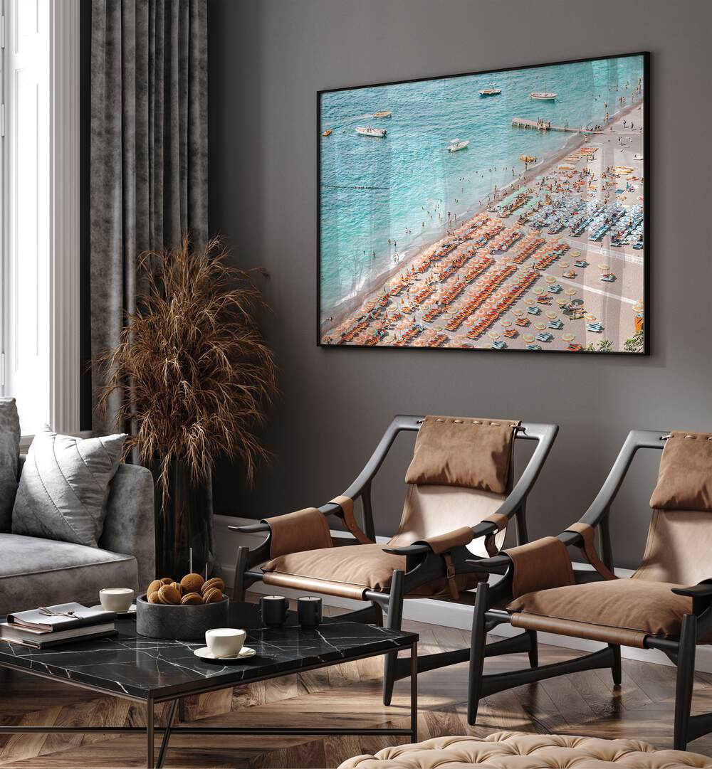 Positano Beach By Grace Digital Art Co Beach Prints in Black Plain Frame placed on a wall behind chairs 