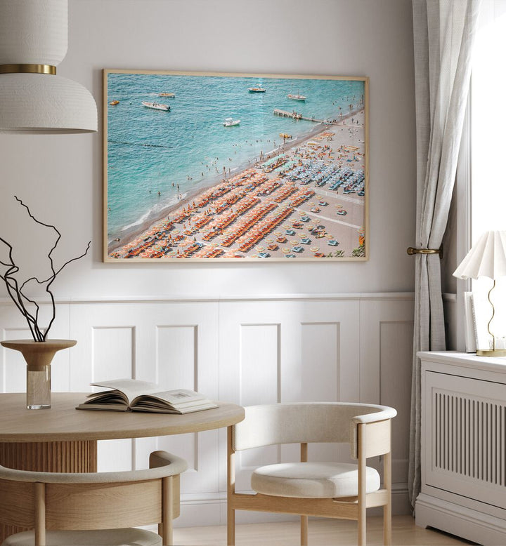 Positano Beach By Grace Digital Art Co Beach Prints in Oak Wood Plain Frame placed on a wall behind a dining table and beside a window