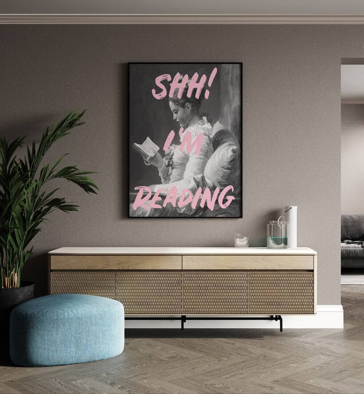 Shh Im Reading By Grace Digital Art Co Altered Art Prints in Black Plain Frame placed on a wall behind a console table and beside a plant