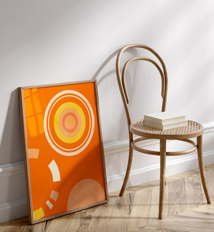 Spring Mid Raphsody Orange IV By Ana Rut Bre Abstract Art Abstract Wall Art in Oak Wood Plain Frame placed on the floor beside a chair