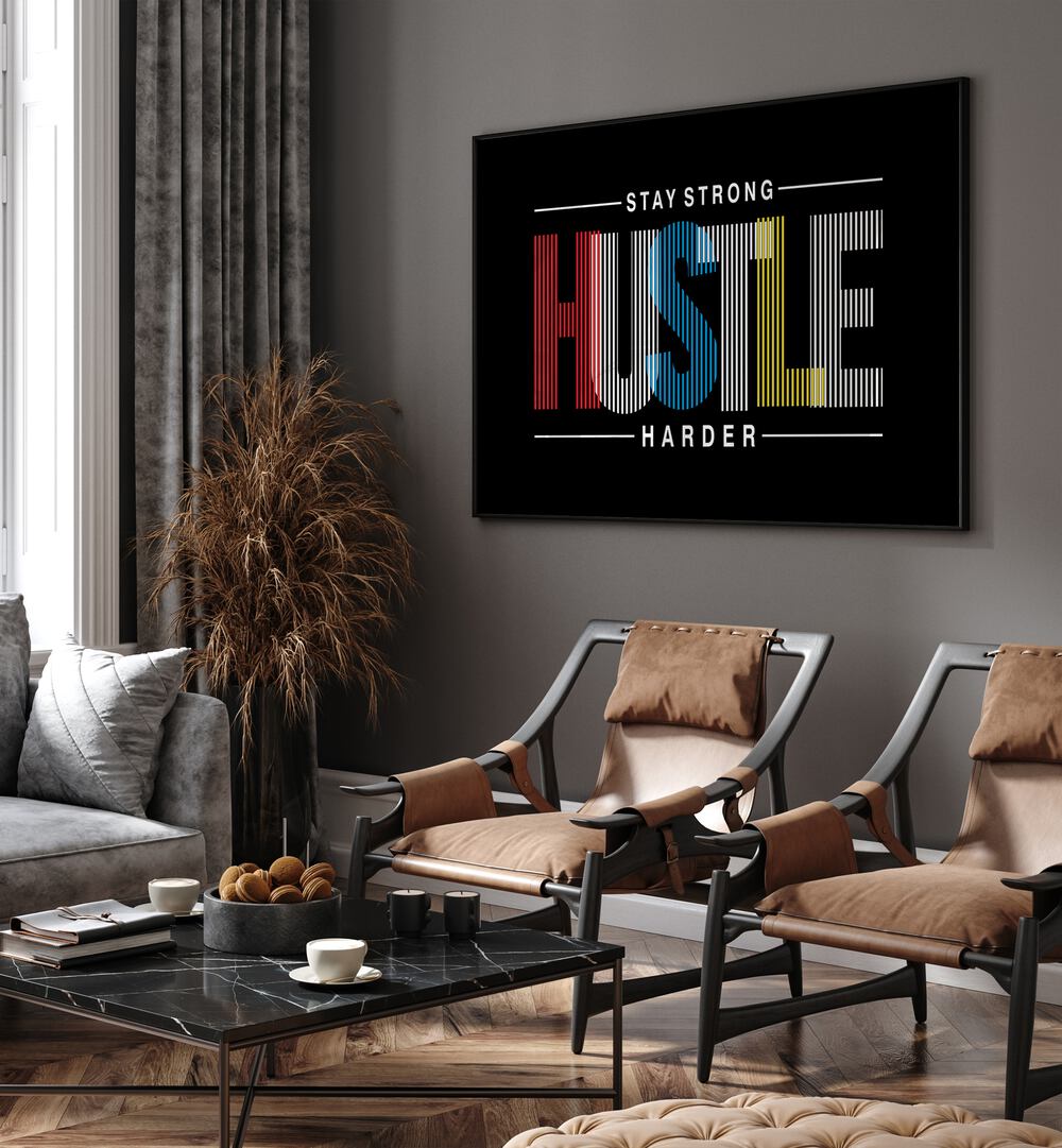 Stay Strong Hustle Harder Quotes and Typography Posters in Black Plain Frame placed on a wall in living room behind chairs