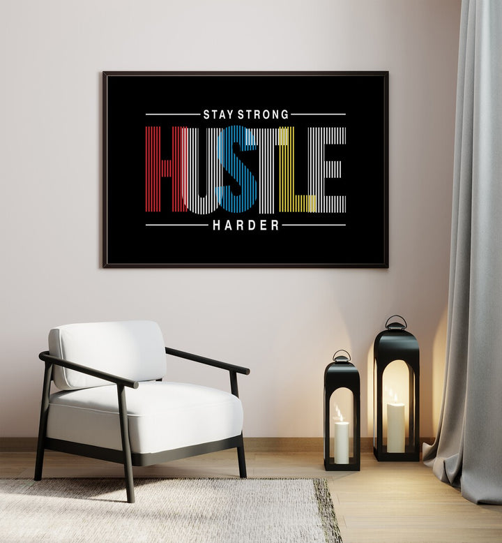 Stay Strong Hustle Harder Quotes and Typography Posters in Black Plain Frame placed on a wall beside a chair