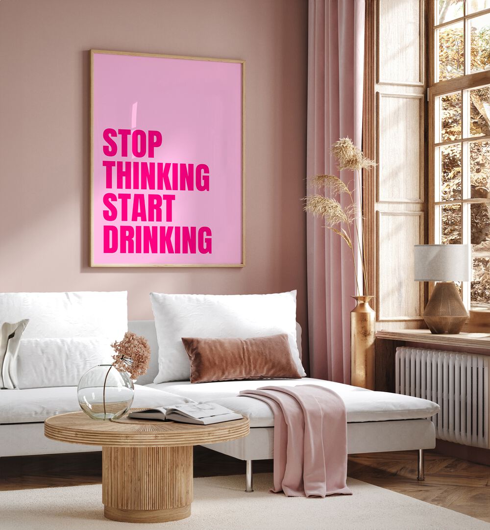 Stop Thinking Start Drinking by Athene Fritsch Quotes and Typography Posters in Oak Wood Plain Frame placed on a pink wall beside a window and behind a sofa for living room