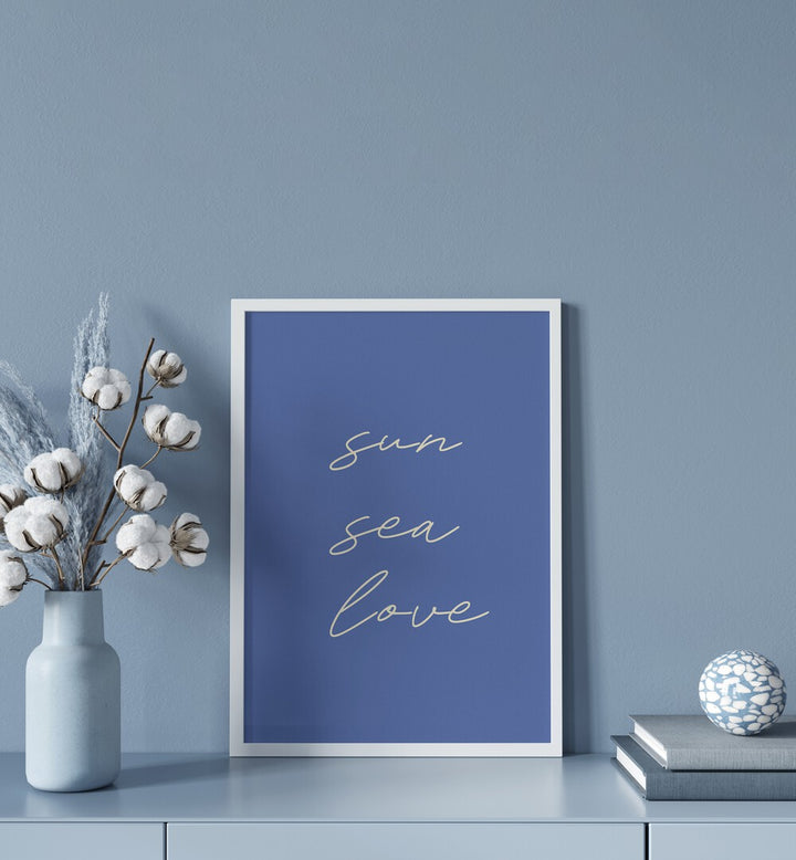 Sun Sea Love Beach Prints Coastal Wall Art in White Plain Frame placed on a Console Table near a Blue Colored Wall