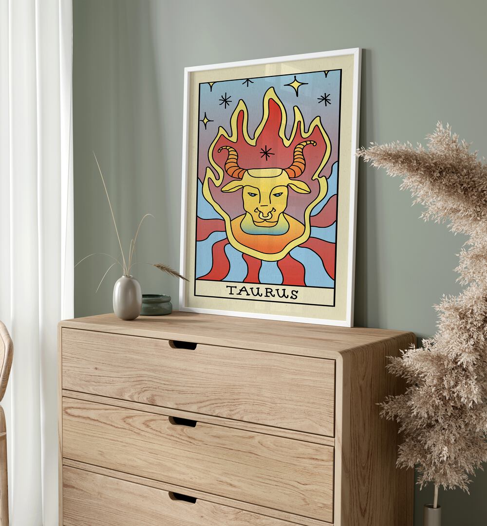 Taurus Zodiac & Tarot Art Painting Artwork in plain white frame on a console table beside a plant