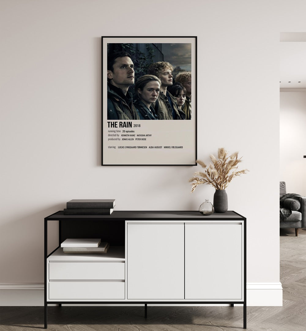 The Rain 2018 Movie Posters in Black Plain Frame placed on a white wall behind a table