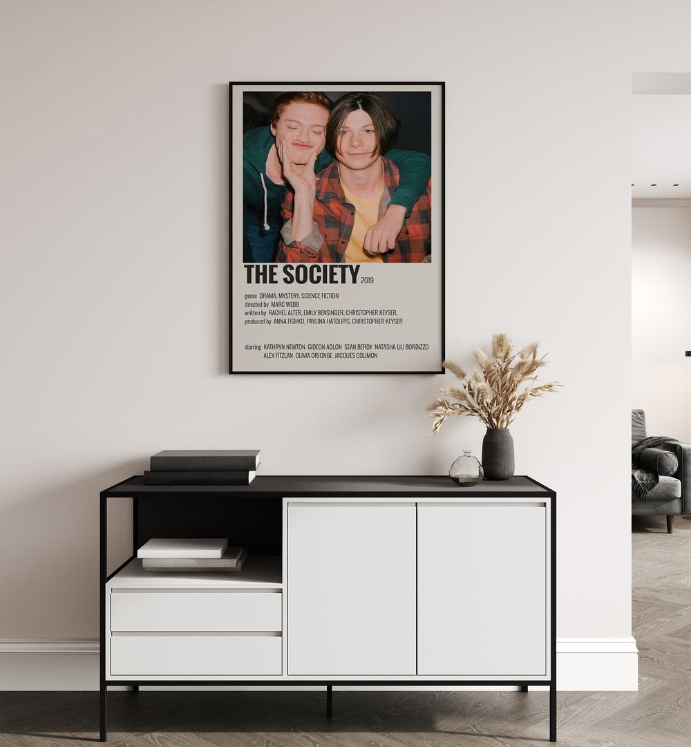 The Society Movie Posters in Black Plain Frame placed on a white wall behind a black and white table