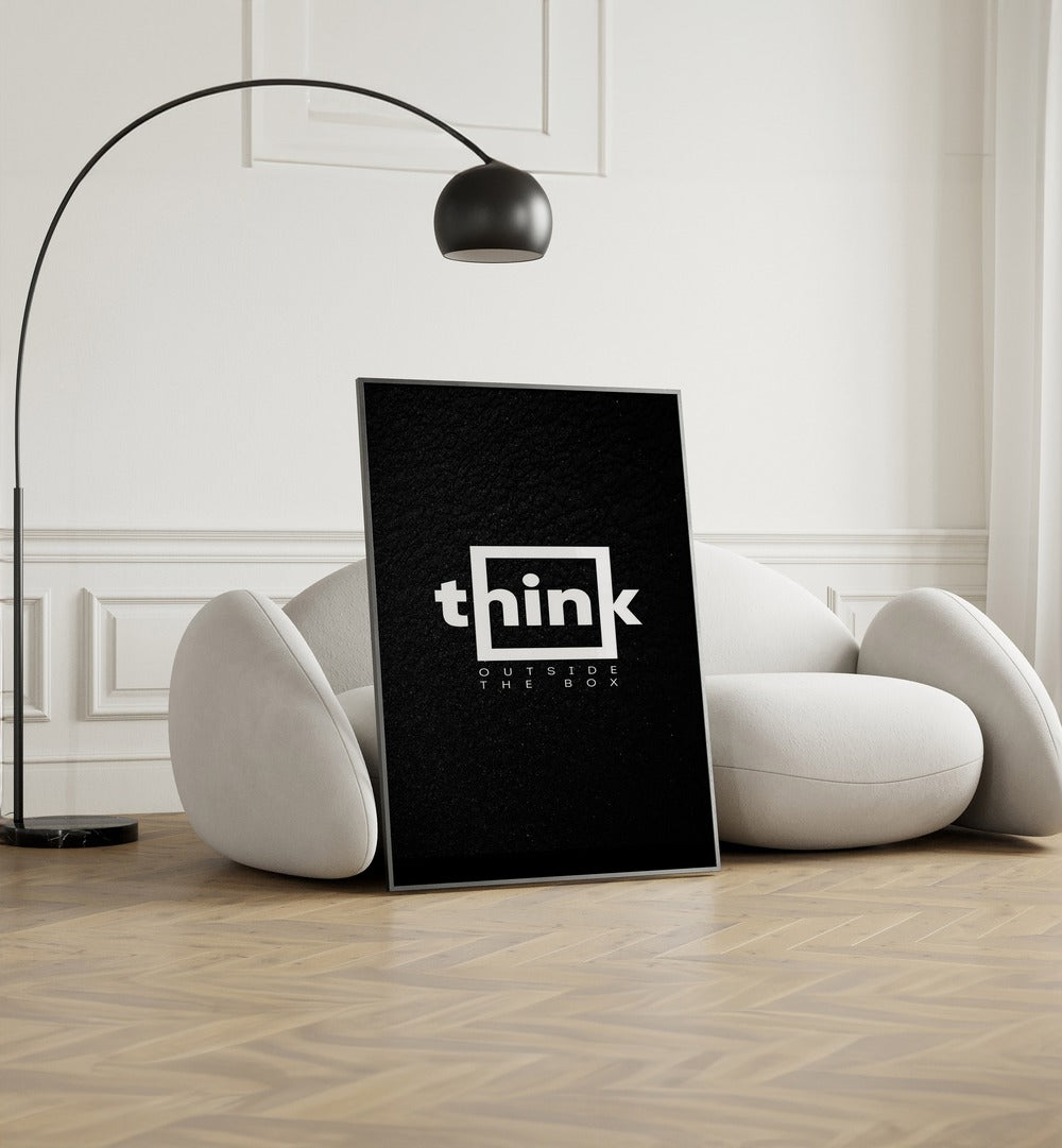 Think Outside The Box Quotes And Typography Posters in Black Plain Frame placed on the floor near a White Sofa in the Living Room