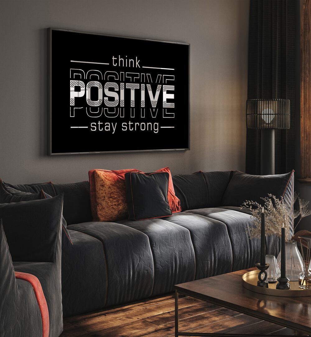 Think Positive Stay Strong Quotes and Typography Posters in Black Plain Frame placed on a wall in a living room behind a sofa