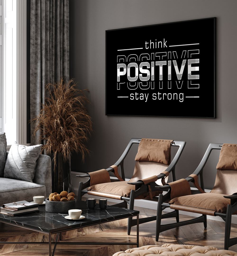 Think Positive Stay Strong Quotes and Typography Posters in Black Plain Frame placed on a wall in living room behind chairs