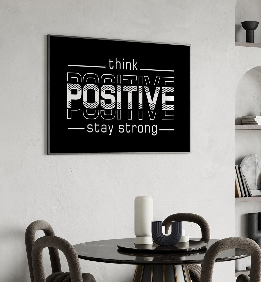 Think Positive Stay Strong Quotes and Typography Posters in Black Plain Frame placed on a wall behind a dining table