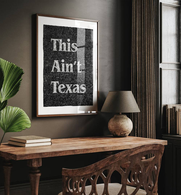 This Aint Texas Quotes And Typography Posters in Dark Wood Plain Frame placed on a Brown Colored Wall  Above a Study Table near a Workspace in the Drawing Room