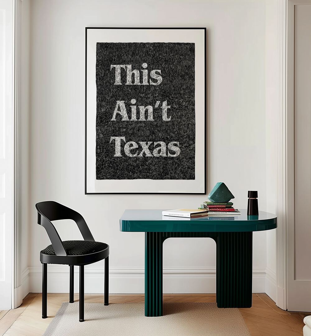 This Aint Texas Quotes And Typography Posters in Black Plain Frame placed on a White Colored Wall Above a Study Table near a Workspace in the Drawing Room