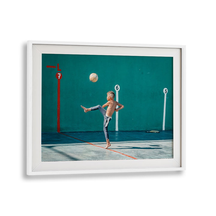 A young boy kicks a yellow ball in vibrant street photography prints, capturing urban life's essence beautifully.