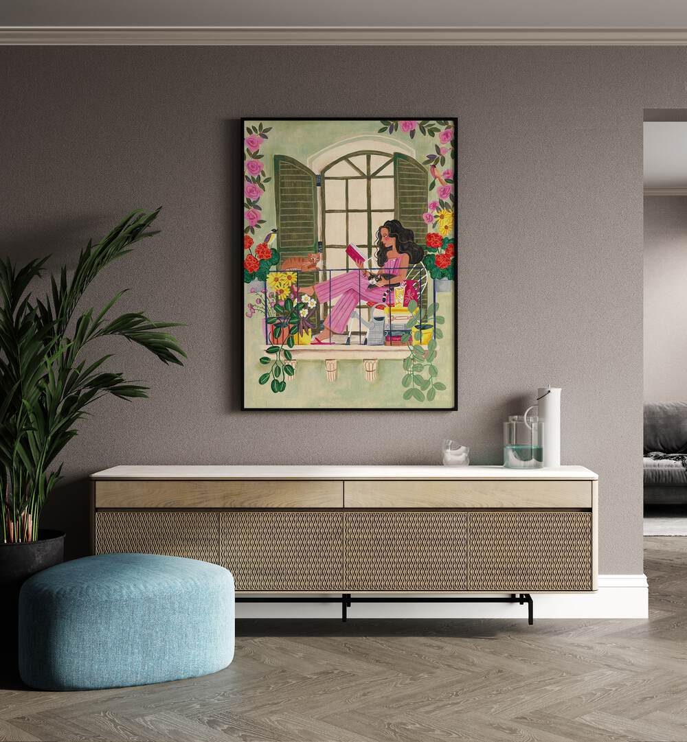 Woman Reads On Balcony By Caroline Bonne Muller Women Illustration Paintings in Black Plain Frame on a wall above a console table beside a plant