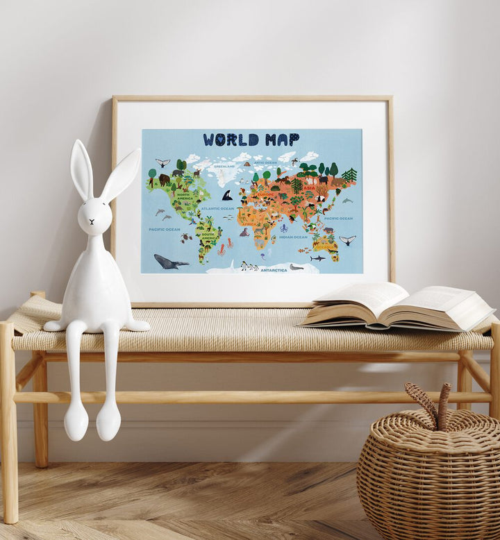 World Map By Jota De Jai Kids Room Art in Oak Wood Frame With Mount on a table beside a toy and a book