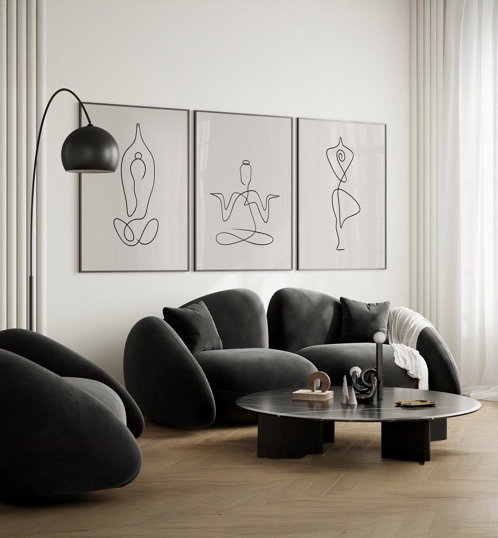 Yoga Line Art Set Set Of 3 Paintings in Black Plain Frame placed on a living room wall behind black sofa and beside a lamp