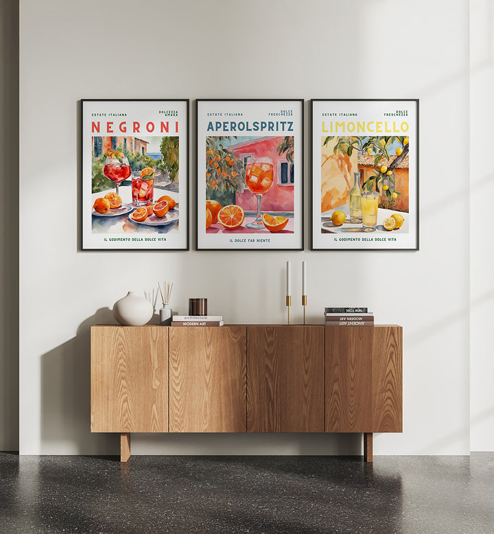 Three framed posters of Negroni, Aperol Spritz, and Limoncello on a wall above a wooden cabinet.