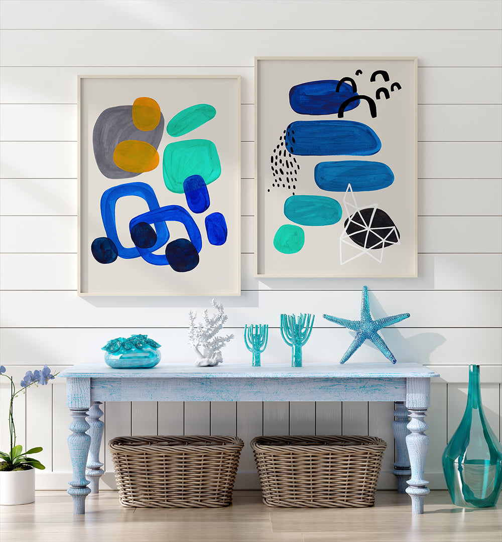 Two abstract art pieces on a wall above a table with decorative items.