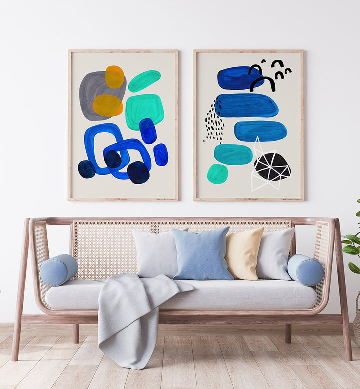 Two abstract art pieces on a wall above a sofa with colorful cushions.